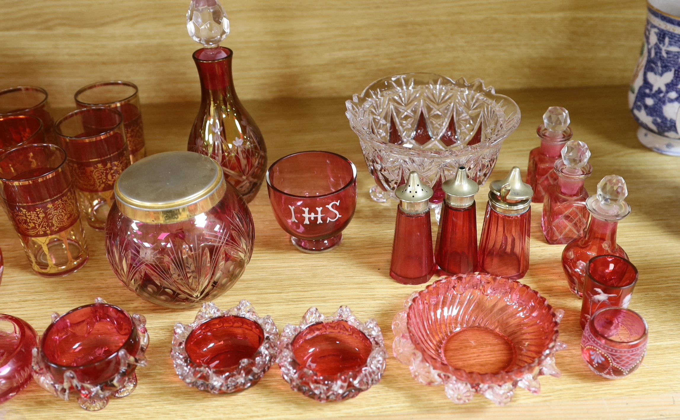 Antique and later cranberry glassware including a biscuit barrel etched with grapevines, Mary Gregory beakers and scent bottle and a vase with enamelled and gilt decoration, the largest 21cm high